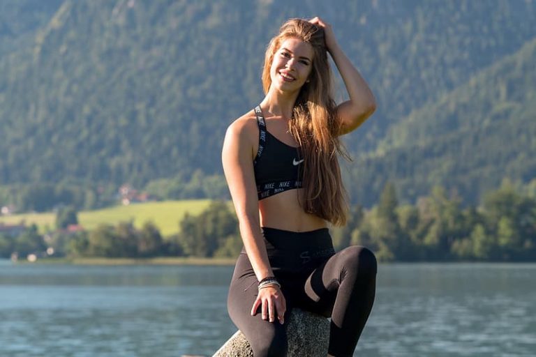 woman-in-black-sports-bra-and-black-leggings-sitting-on-rock-near-body-of-water-during