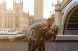 a man and woman kissing in front of a clock tower