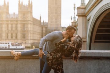 a man and woman kissing in front of a clock tower