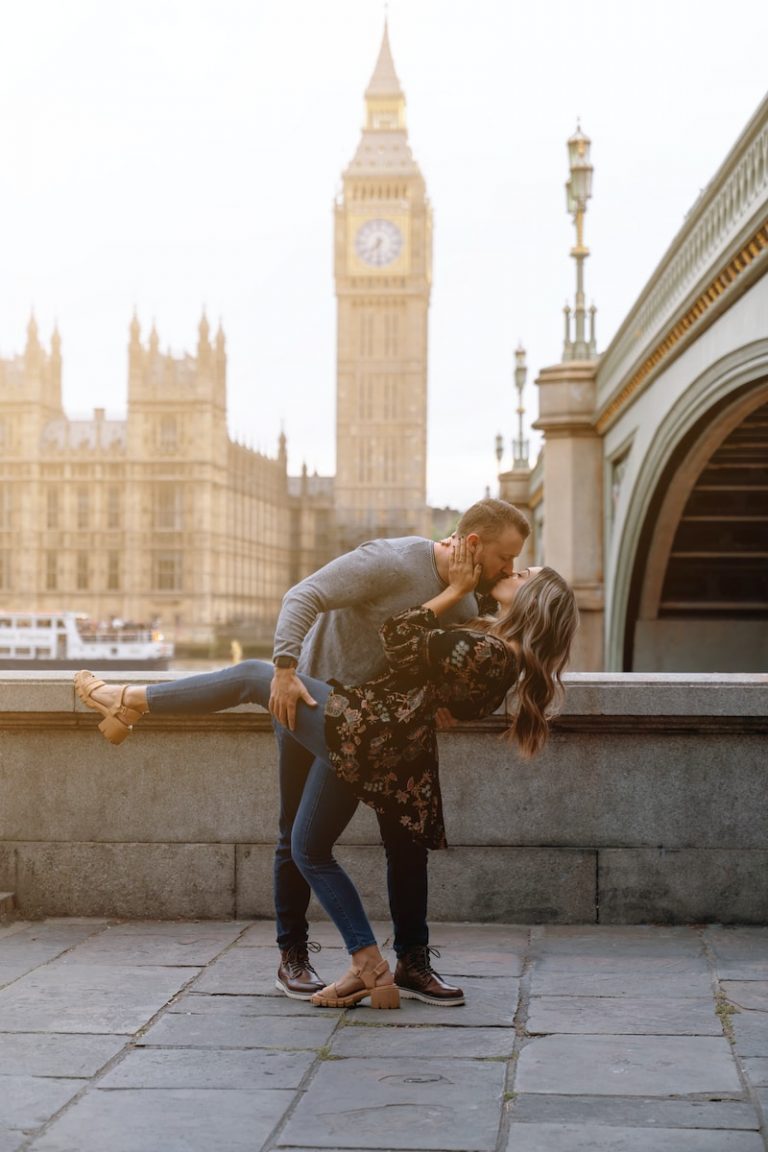 a man and woman kissing in front of a clock tower