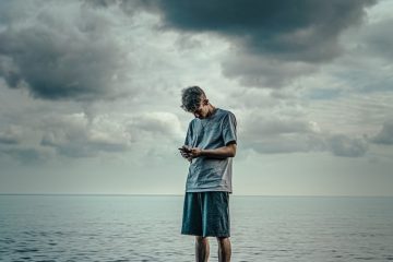 woman in white long sleeve shirt and blue skirt standing on rock in front of sea