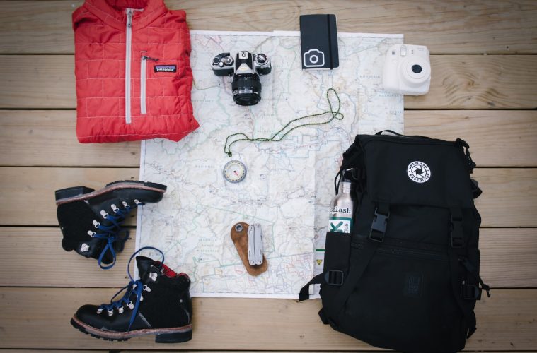 black hiking backpack near white Fujifilm instax mini camera near black leather boots, red half-zip jacket, gray pocket watch on white map