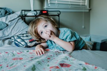 boy lying on bed while raising left hand near his mouth