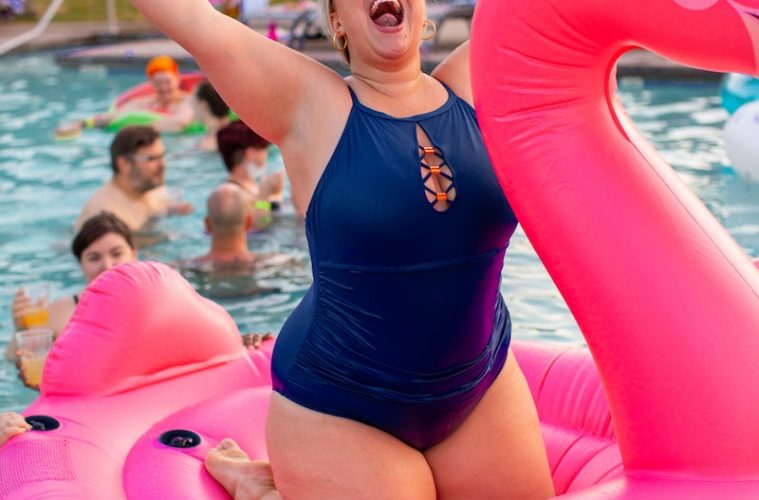 woman wearing blue swimsuit knee on pink flamingo floaters during daytime