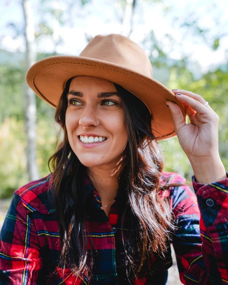 smiling woman in red and blue plaid dress shirt wearing brown hat